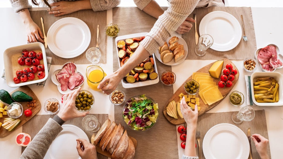 Overhead view of a diverse cheese platter setup for a delicious meal, featuring fresh produce and juices on a table.